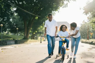 Man Standing Beside His Wife Teaching Their Child How to Ride Bicycle