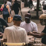 Men Sitting Beside Table on Pathway Near People Walking Beside Rail