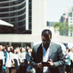 Selective Focus Photography of Man Holding Smartphone While Standing Near People