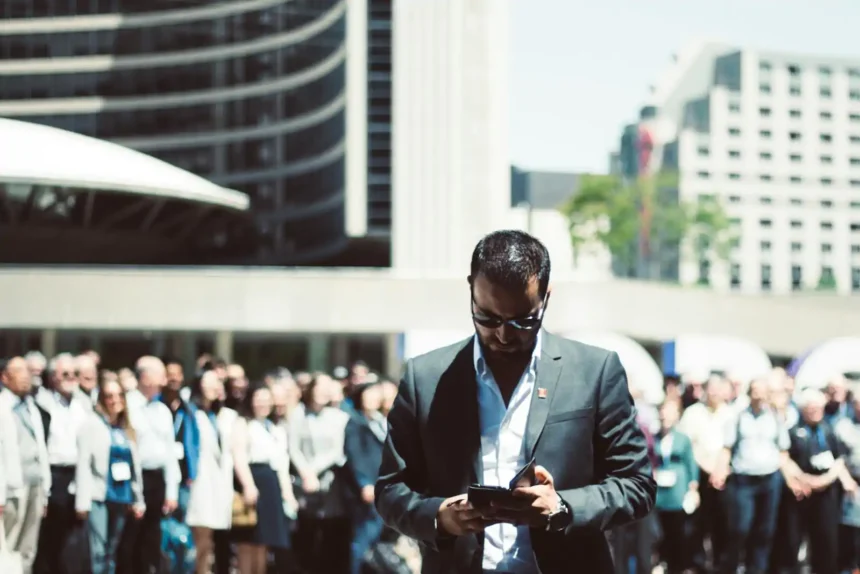 Selective Focus Photography of Man Holding Smartphone While Standing Near People