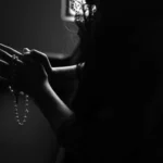 silhouette of woman holding rosary while praying