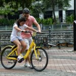 Roles Of The Father In The Family: Father teaches daughter to ride a yellow bicycle in a Singapore park. Bonding moment.