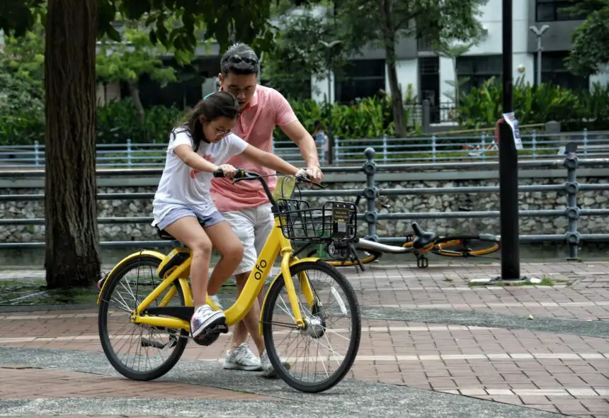 Roles Of The Father In The Family: Father teaches daughter to ride a yellow bicycle in a Singapore park. Bonding moment.