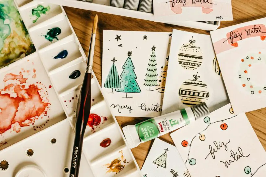 Introduction to Pattern and Card Making: Artistic holiday card designs with watercolor paints and brushes on a wooden table.