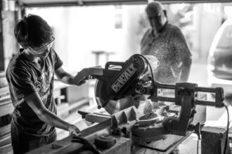 Trades where apprenticeship system is practiced: grayscale photography of boy using miter saw