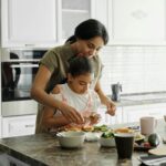 Roles Of The Mother In The Family: A mom and daughter share a bonding moment while preparing a healthy lunch together in the kitchen.