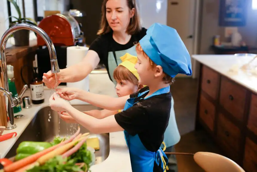 Roles Of The Children In The Family: Mother and children wearing chef hats washing hands while preparing food together in the kitchen.