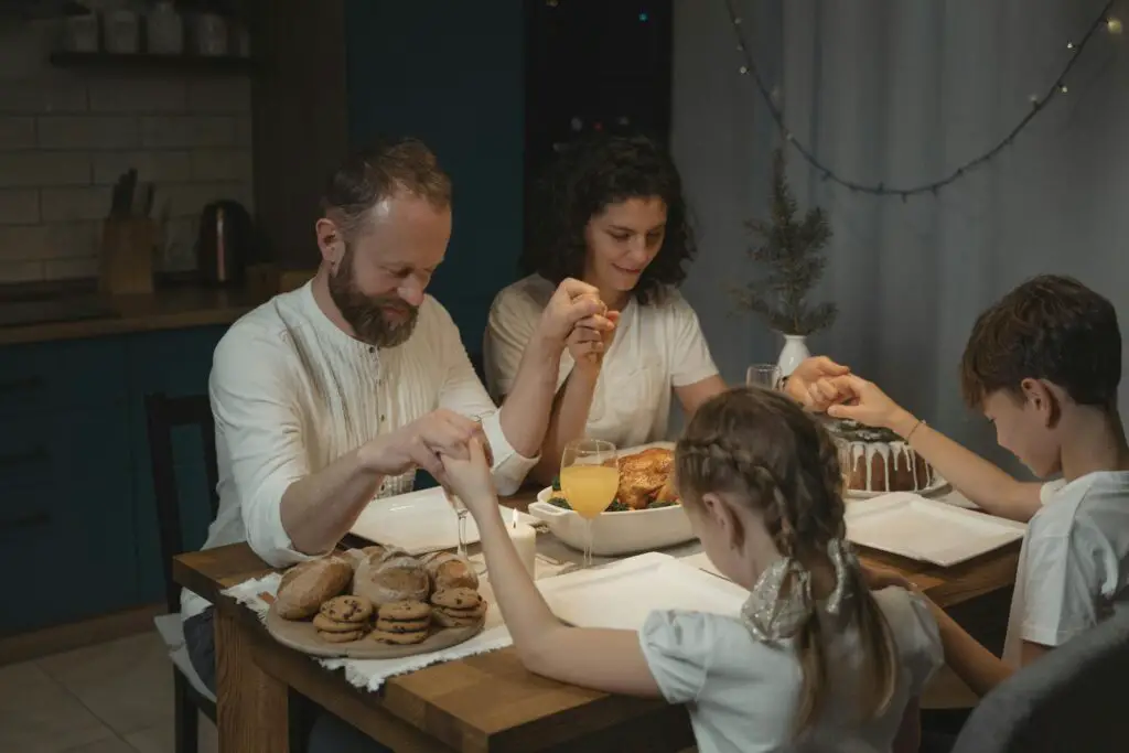 Family values: holding hands and praying over a dinner table with turkey and cookies during festival celebration.